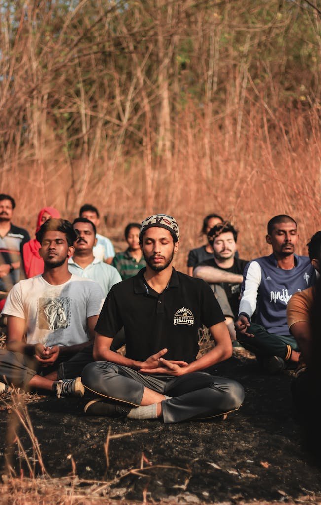 A diverse group meditating outdoors in a natural setting in Thrissur, India, promoting peace and relaxation.
